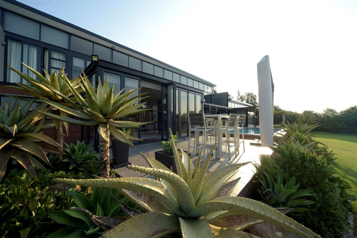 A modern rear exterior featuring a tiled patio, swimming pool, and expansive bi-fold glass doors connecting the indoor and outdoor living spaces.