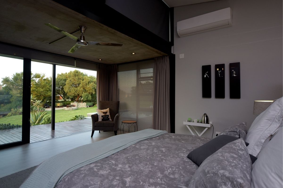 Modern bedroom featuring an exposed concrete ceiling, split-system air conditioning, and large sliding glass doors opening onto a wooden deck and garden.