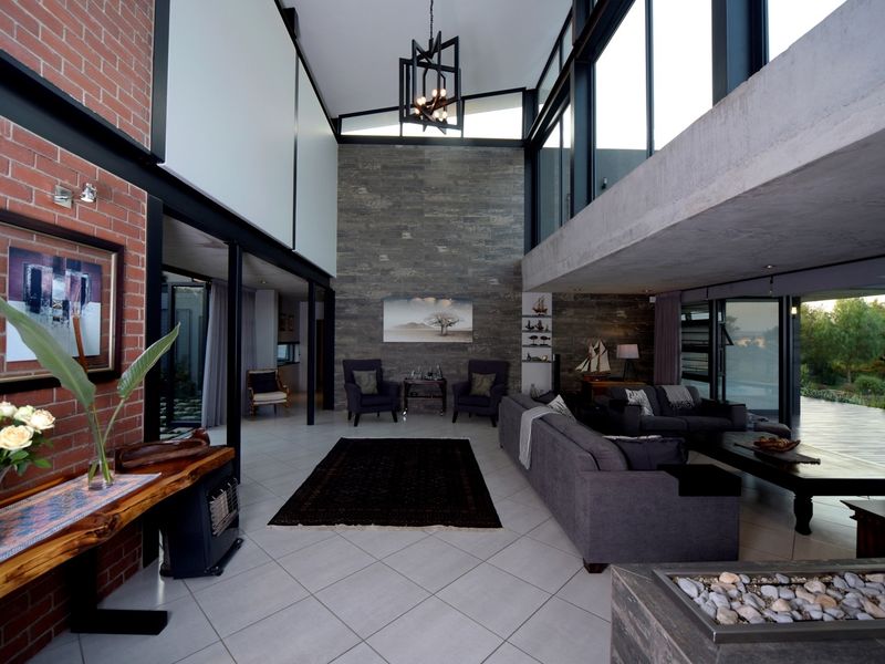 Spacious open-plan living area featuring high vaulted ceilings, exposed brick and stone walls, and large windows overlooking the outdoor space.