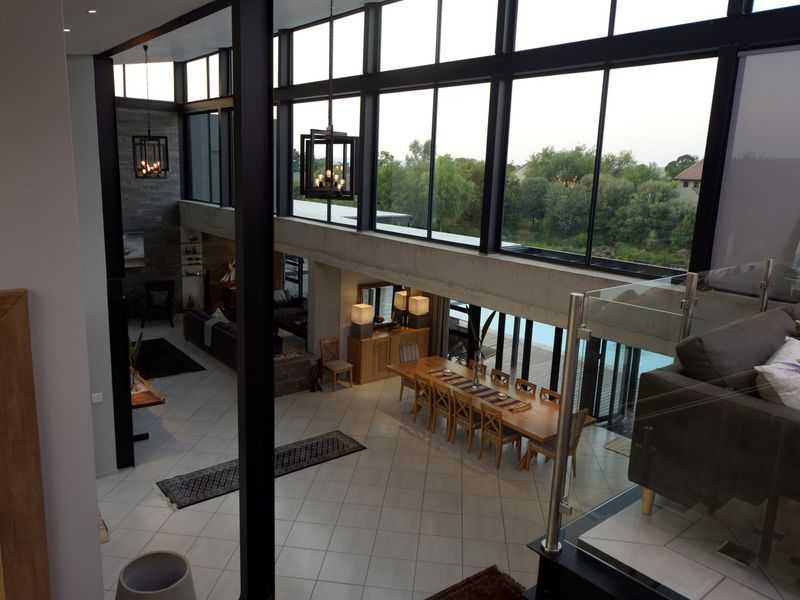 Spacious open-plan living and dining area featuring double-volume ceilings, extensive floor-to-ceiling windows, and modern architectural finishes with views of the pool area.