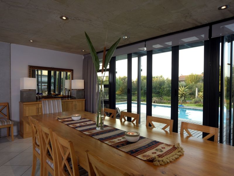 Spacious dining area featuring an exposed concrete ceiling, recessed lighting, and large black aluminium stacker doors opening onto a pool deck.