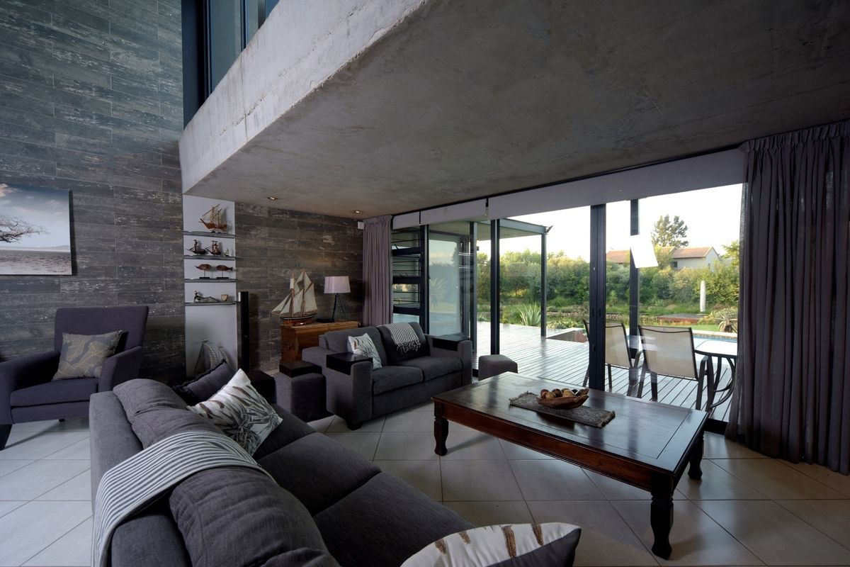Spacious living room featuring an exposed concrete ceiling, stone feature wall, and large sliding glass doors that open onto an outdoor deck.