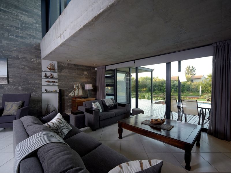 Spacious living room featuring an exposed concrete ceiling, stone feature wall, and large sliding glass doors that open onto an outdoor deck.
