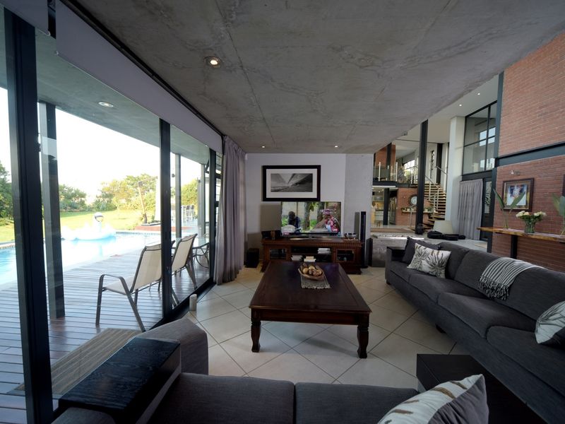 Spacious open-plan living area featuring exposed concrete ceilings, brick feature walls, and large sliding glass doors opening onto a pool deck.