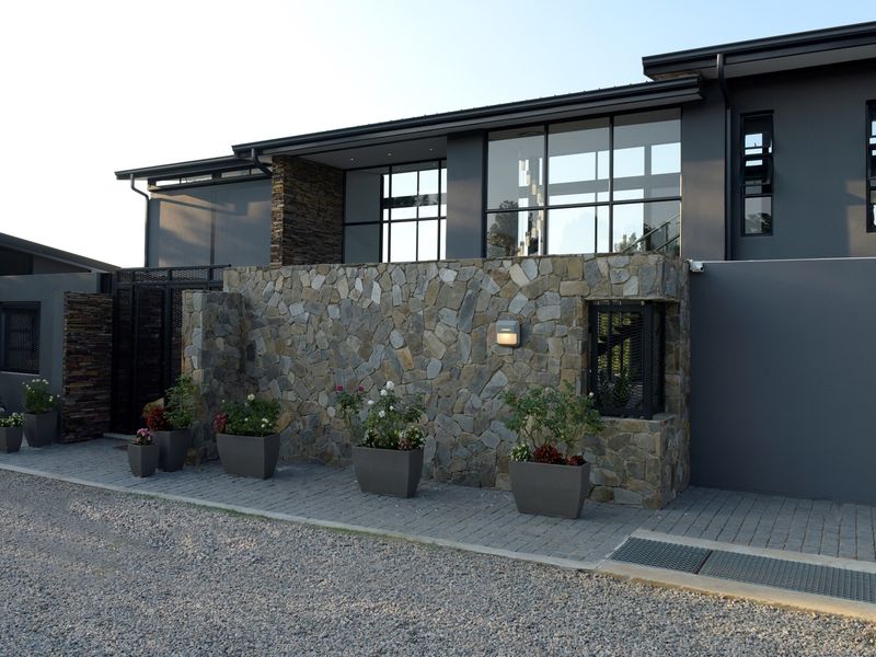 Modern architectural facade featuring stone cladding, large glass windows, and a paved entrance area with contemporary dark exterior finishes.