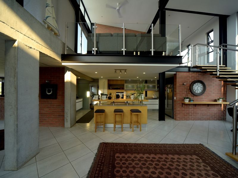 Spacious open-plan living area featuring industrial design elements, exposed brickwork, steel beams, a mezzanine level with glass balustrade, and a modern kitchen island.
