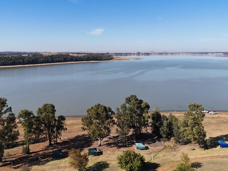 An aerial view of the vacant residential land featuring extensive lake frontage and established mature trees, offering scenic water views.