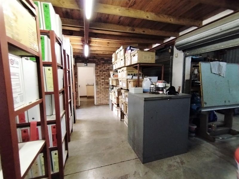 Industrial storage or utility space featuring exposed timber ceiling beams, brickwork accents, concrete flooring, and a roller shutter door access point.