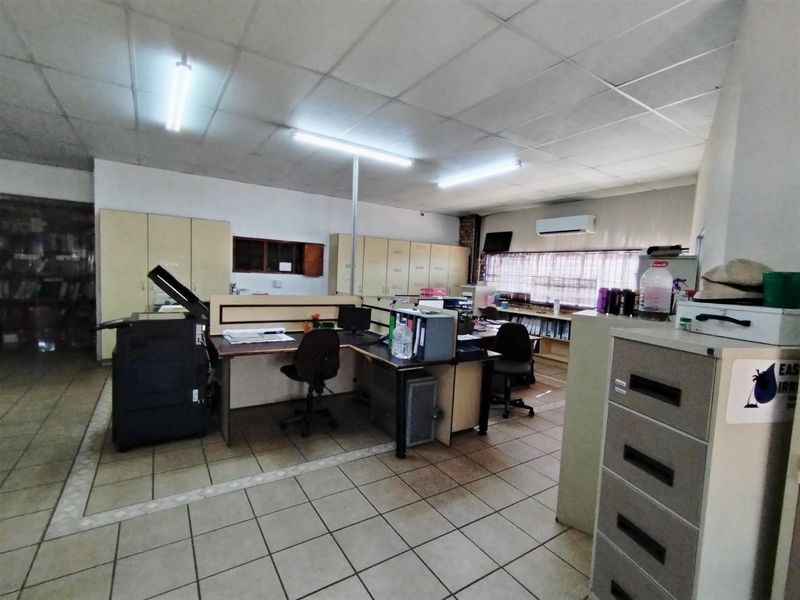Functional office space featuring built-in cabinetry, tiled flooring, suspended ceiling with fluorescent lighting, and a wall-mounted air conditioning unit.