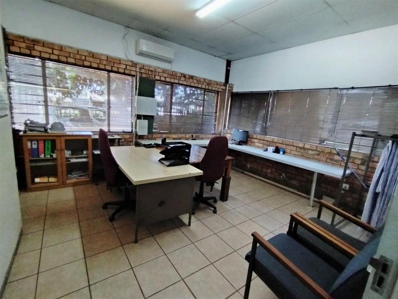 Functional office space featuring exposed brick walls, tiled flooring, integrated air conditioning unit, and large windows with fitted blinds.