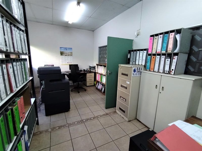 Functional office space featuring tiled flooring, fluorescent lighting, and built-in storage shelving, suitable for administrative or industrial operations.