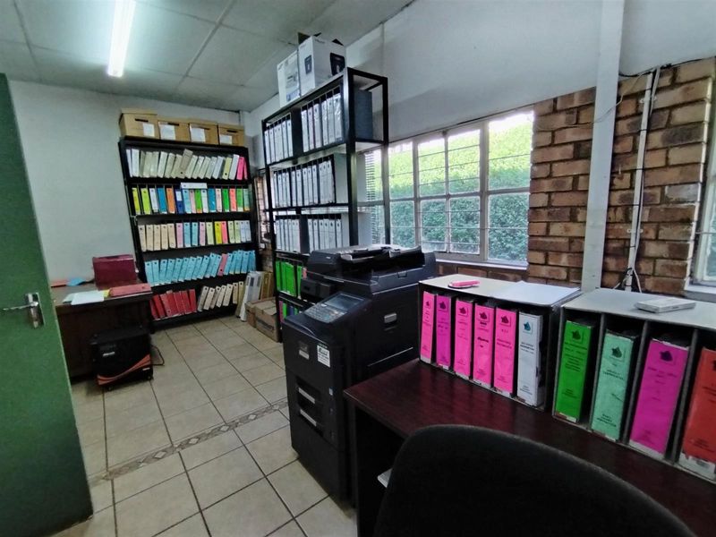 Functional office space featuring exposed brickwork, tiled flooring, and large windows providing natural light, suitable for administrative or industrial operations.