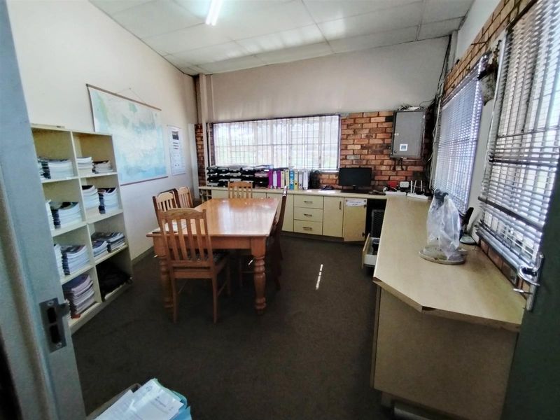 Functional office space featuring exposed brick walls, built-in cabinetry, and large windows with blinds, suitable for administrative or industrial workspace use.