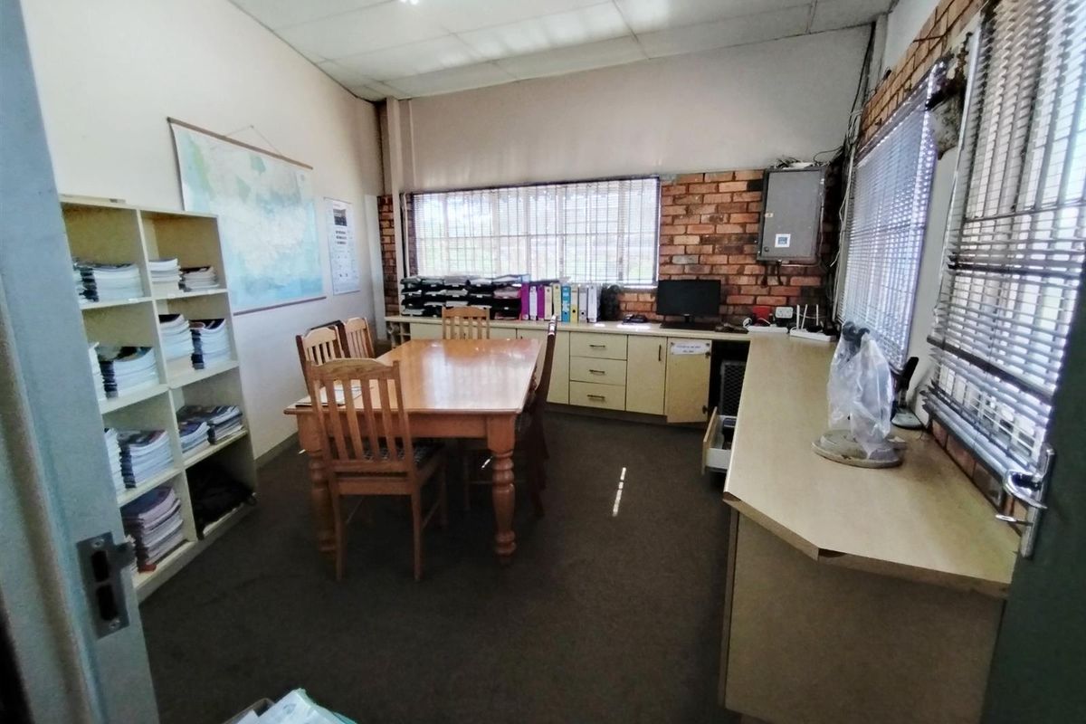 Functional office space featuring exposed brick walls, built-in cabinetry, and large windows with blinds, suitable for administrative or industrial workspace use.