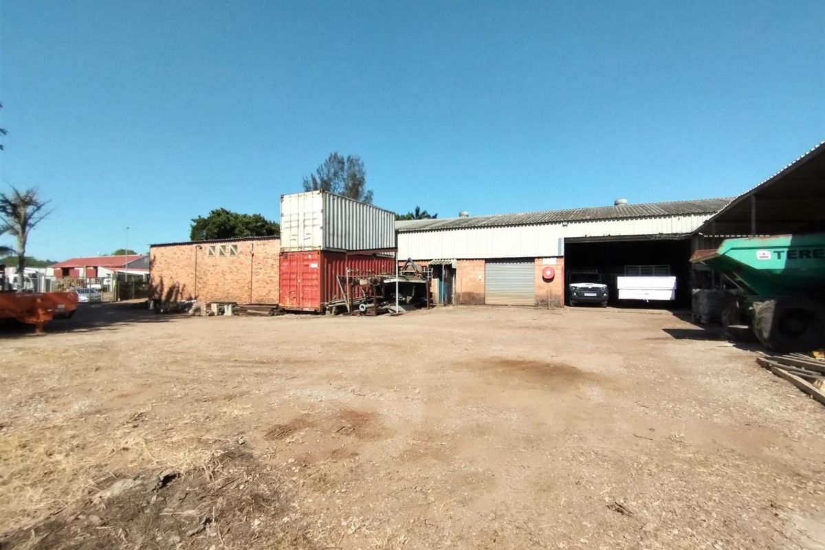 Industrial property exterior featuring a large unpaved yard area, brick warehouse structure, and roller shutter door access.