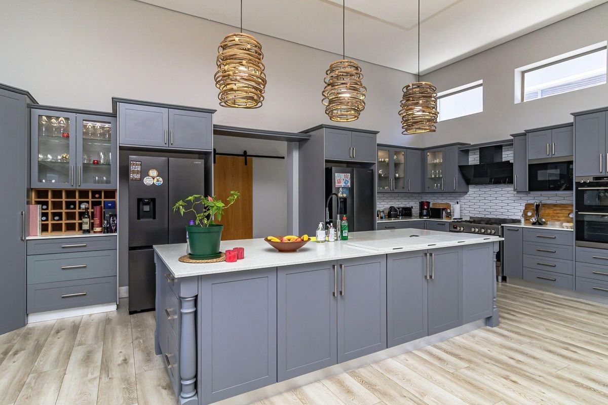 Modern kitchen featuring grey cabinetry, a large central island with stone countertops, built-in oven, extractor fan, and high ceilings with pendant lighting.