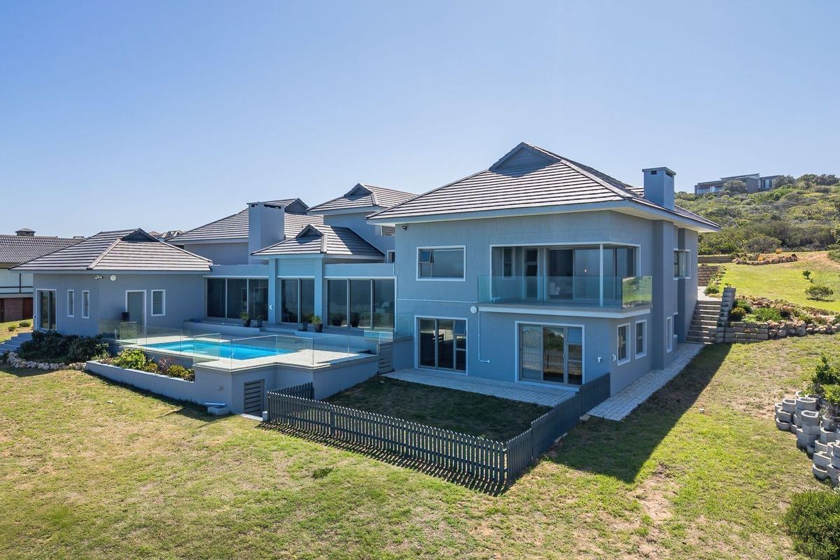 Aerial view of a modern multi-level residence featuring a swimming pool, glass balustrades, tiled roof, and expansive rear garden area.