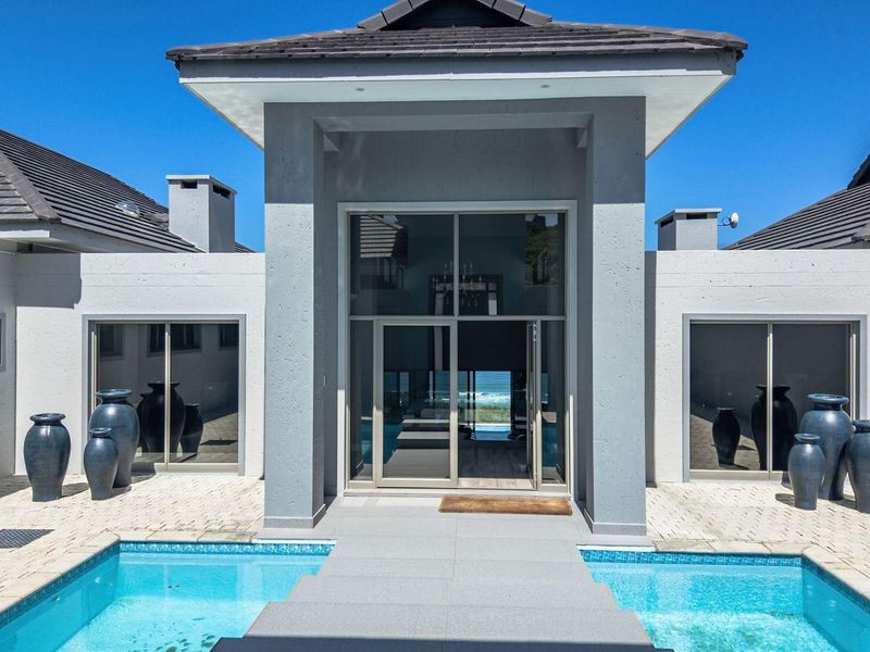A modern architectural entrance featuring a central walkway over a swimming pool, flanked by symmetrical wings with large sliding glass doors.