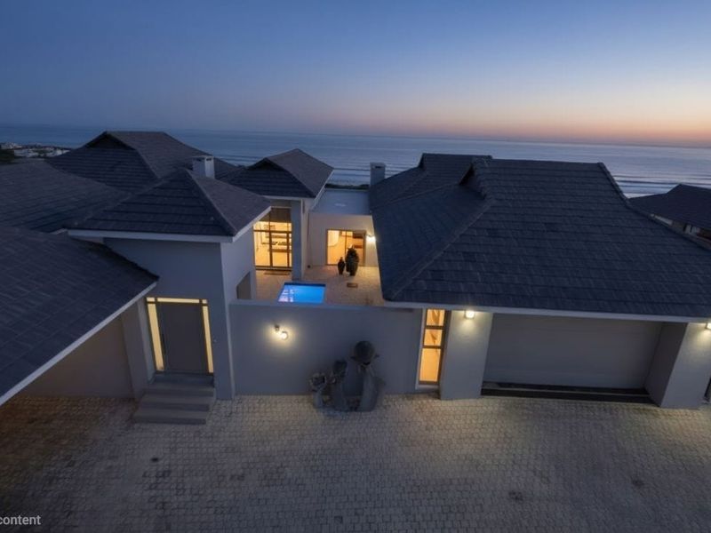 Aerial view of a modern coastal residence at dusk, featuring a paved driveway, integrated garage, and a central courtyard with a swimming pool.