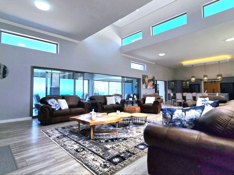 Spacious open-plan living and dining area featuring vaulted ceilings, clerestory windows, modern laminate flooring, and large sliding glass doors leading to the outdoors.