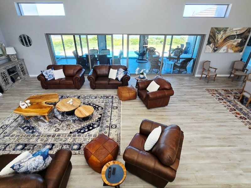 Spacious open-plan living area featuring high ceilings, clerestory windows, wood-look tile flooring, and large sliding glass doors leading to an outdoor patio.