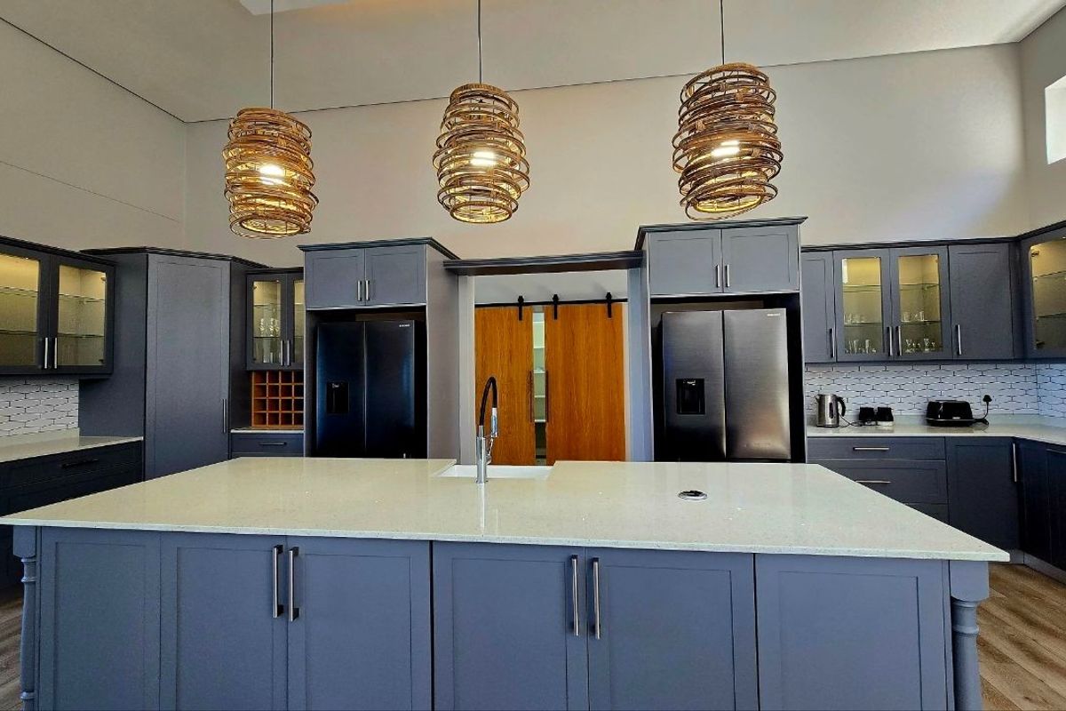 Modern kitchen featuring dark grey cabinetry, a large central island with quartz countertops, and elegant pendant lighting.