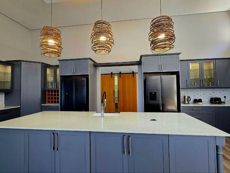 Modern kitchen featuring dark grey cabinetry, a large central island with quartz countertops, and elegant pendant lighting.