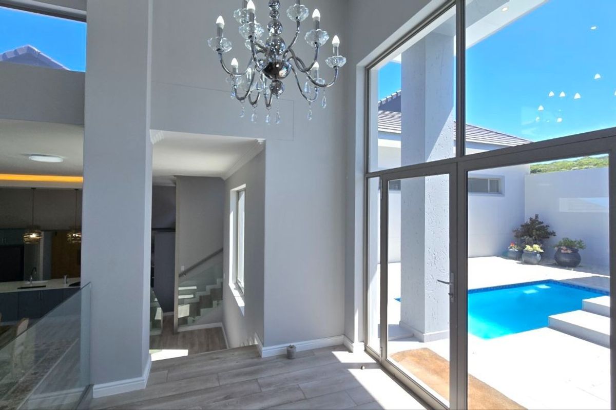 Spacious living area featuring high ceilings, modern chandelier, and expansive glass doors providing seamless access to the outdoor pool area.