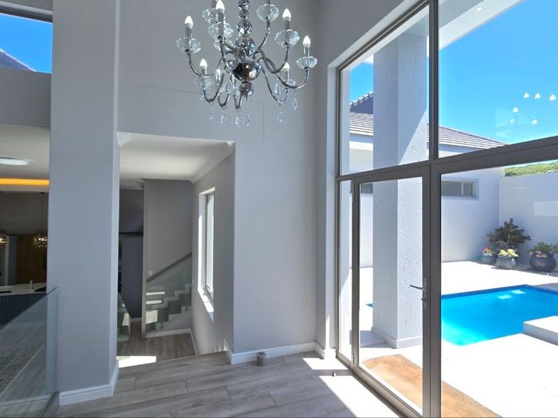 Spacious living area featuring high ceilings, modern chandelier, and expansive glass doors providing seamless access to the outdoor pool area.