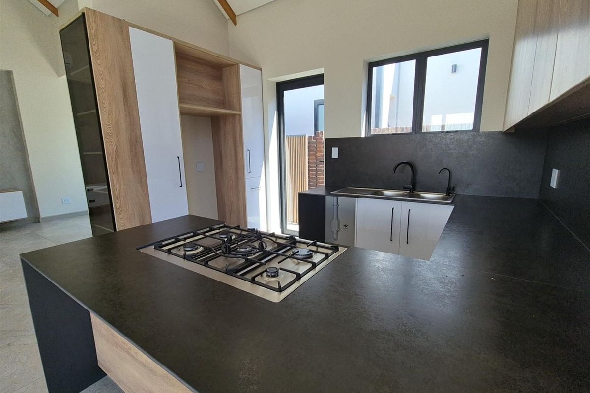 Modern kitchen featuring dark stone countertops, integrated gas hob, double sink with matte black fixtures, and contemporary wood-grain cabinetry with high-ceiling architecture.