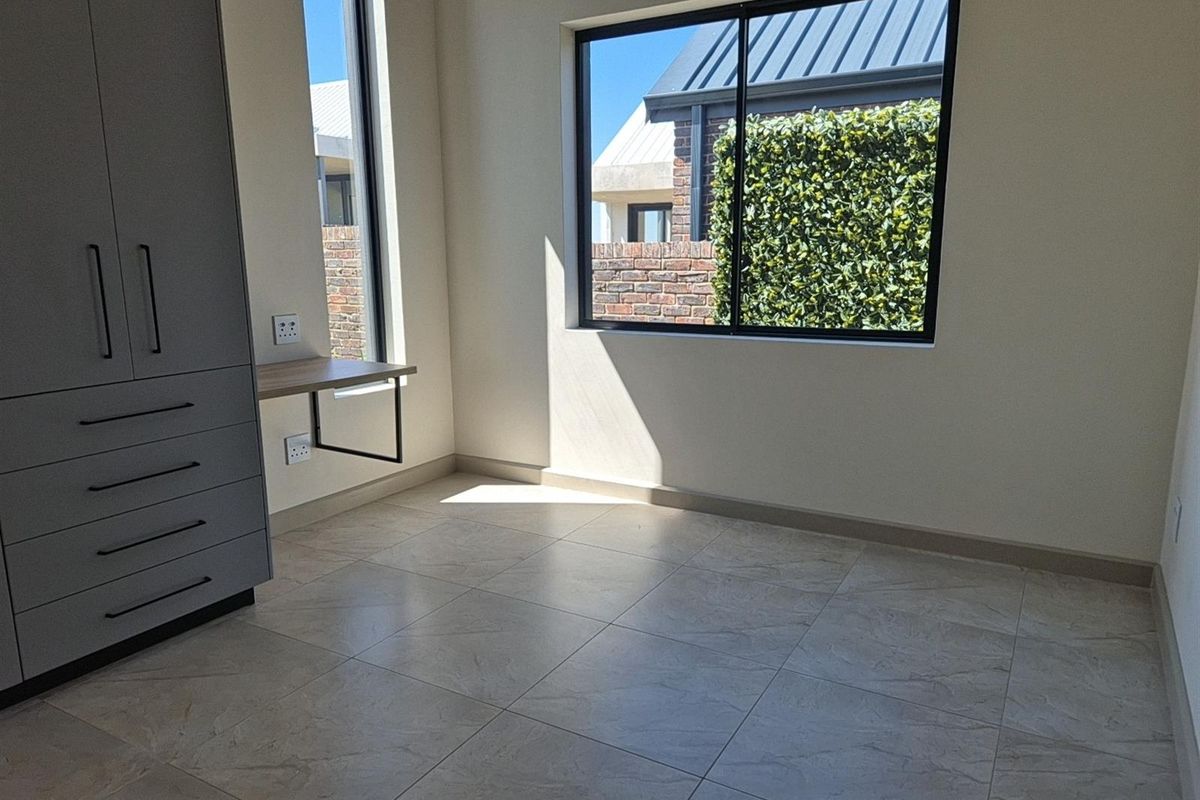 A bright, modern bedroom featuring tiled flooring, built-in cabinetry, and a floating desk area with large windows providing natural light.