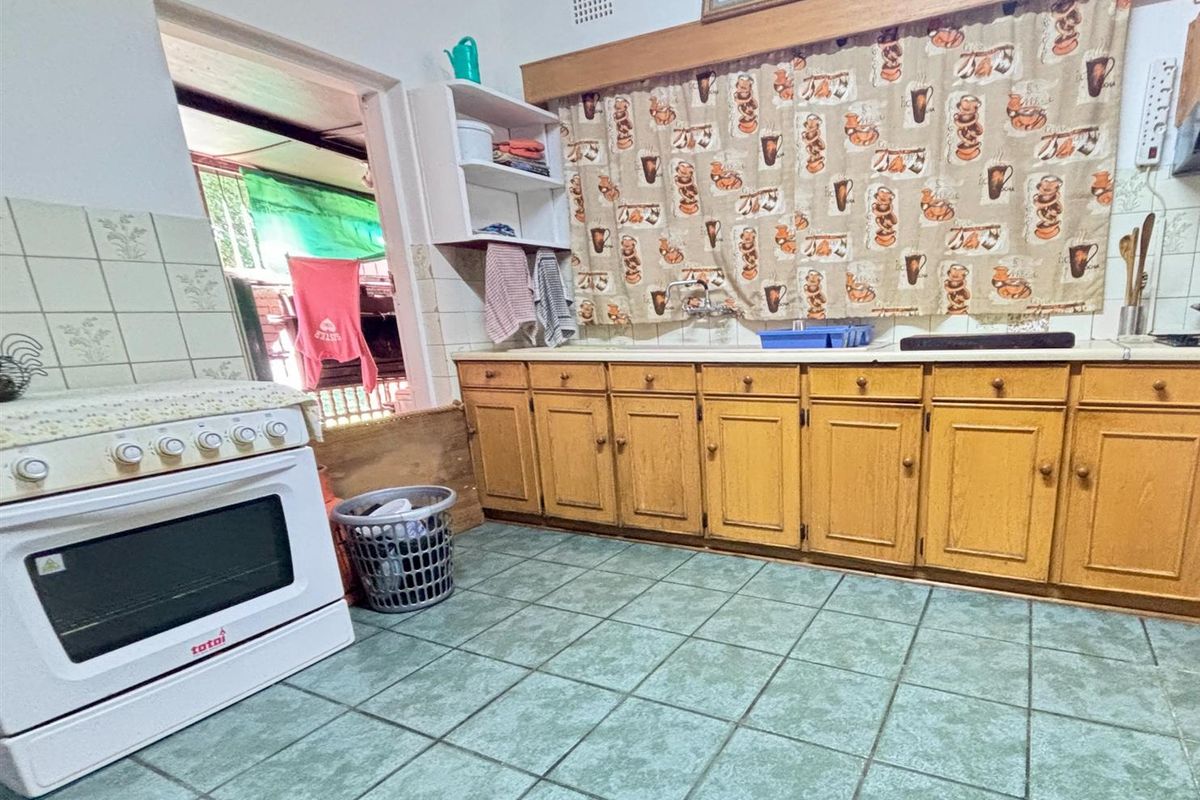 A dated kitchen featuring wooden cabinetry, tiled flooring, and a freestanding stove, offering a functional space with potential for modernization.
