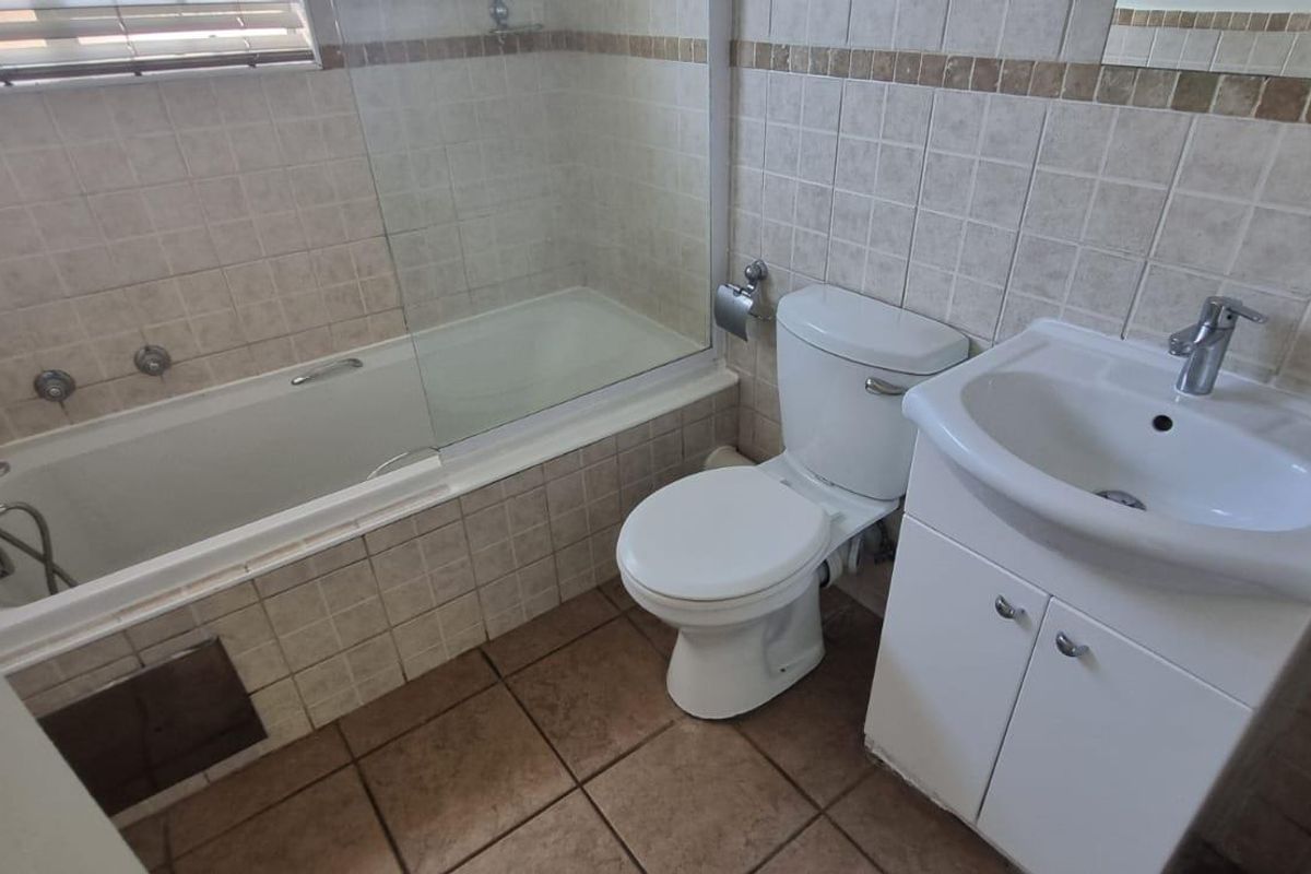 A functional bathroom featuring a bathtub with a glass shower screen, a pedestal vanity with a basin, and a standard toilet.