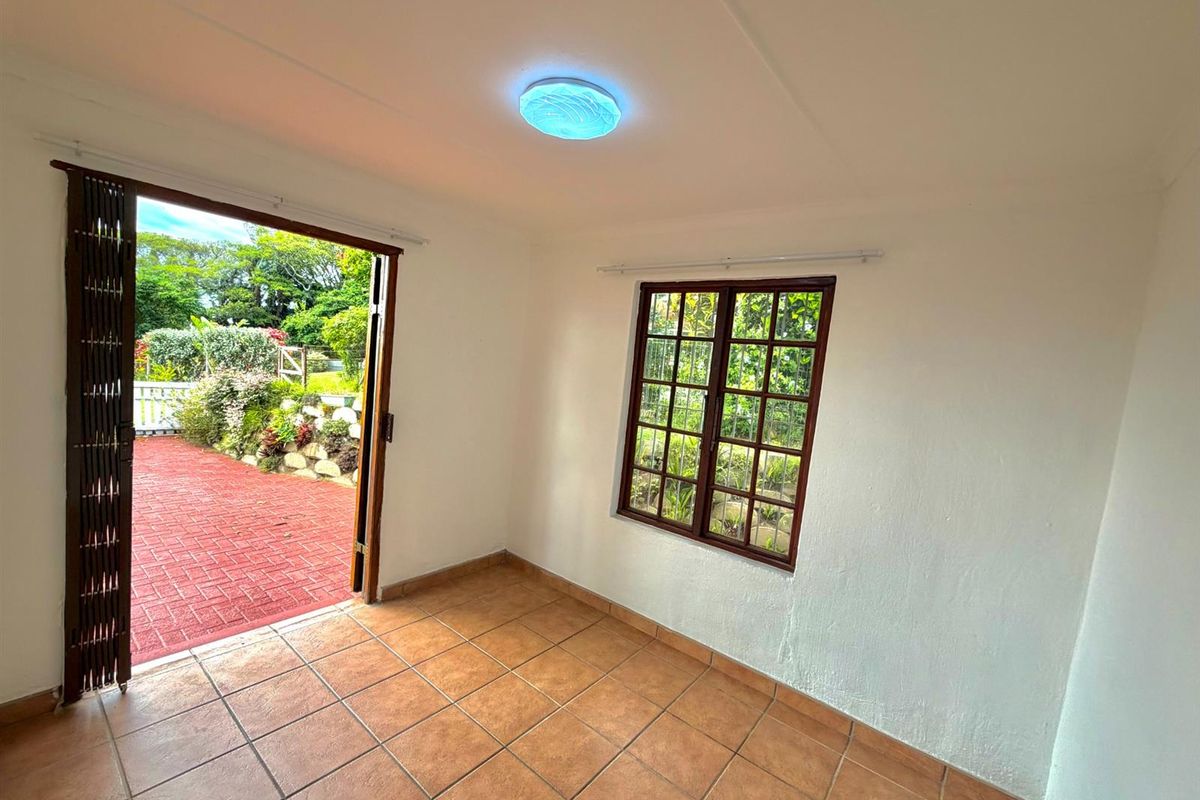 An empty living room featuring tiled flooring, a wooden window, and a folding door providing direct access to the outdoor patio area.