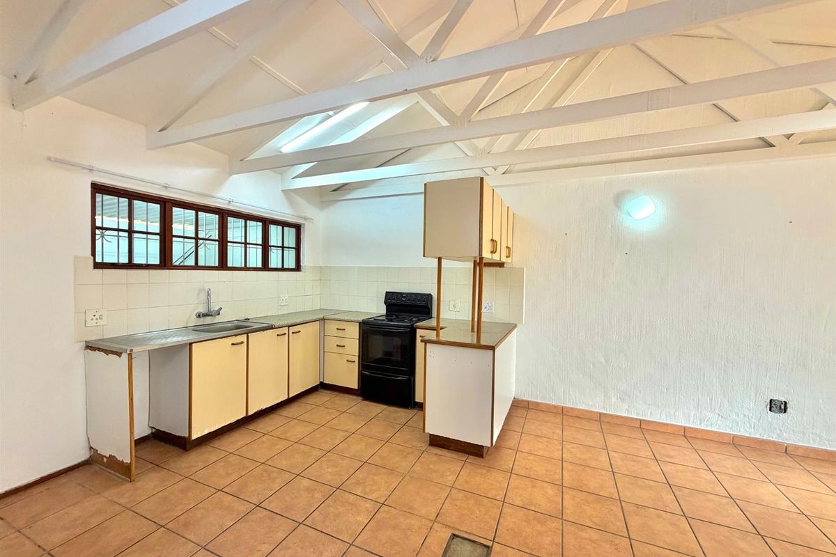 Empty kitchen featuring exposed white timber rafters, tiled flooring, built-in cabinetry, and a skylight, offering a blank canvas for renovation.