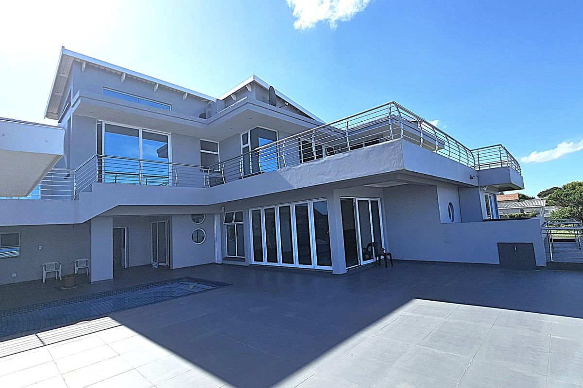 A spacious rear exterior view of a modern multi-level home featuring a large tiled patio, swimming pool, and stainless steel balcony railings.