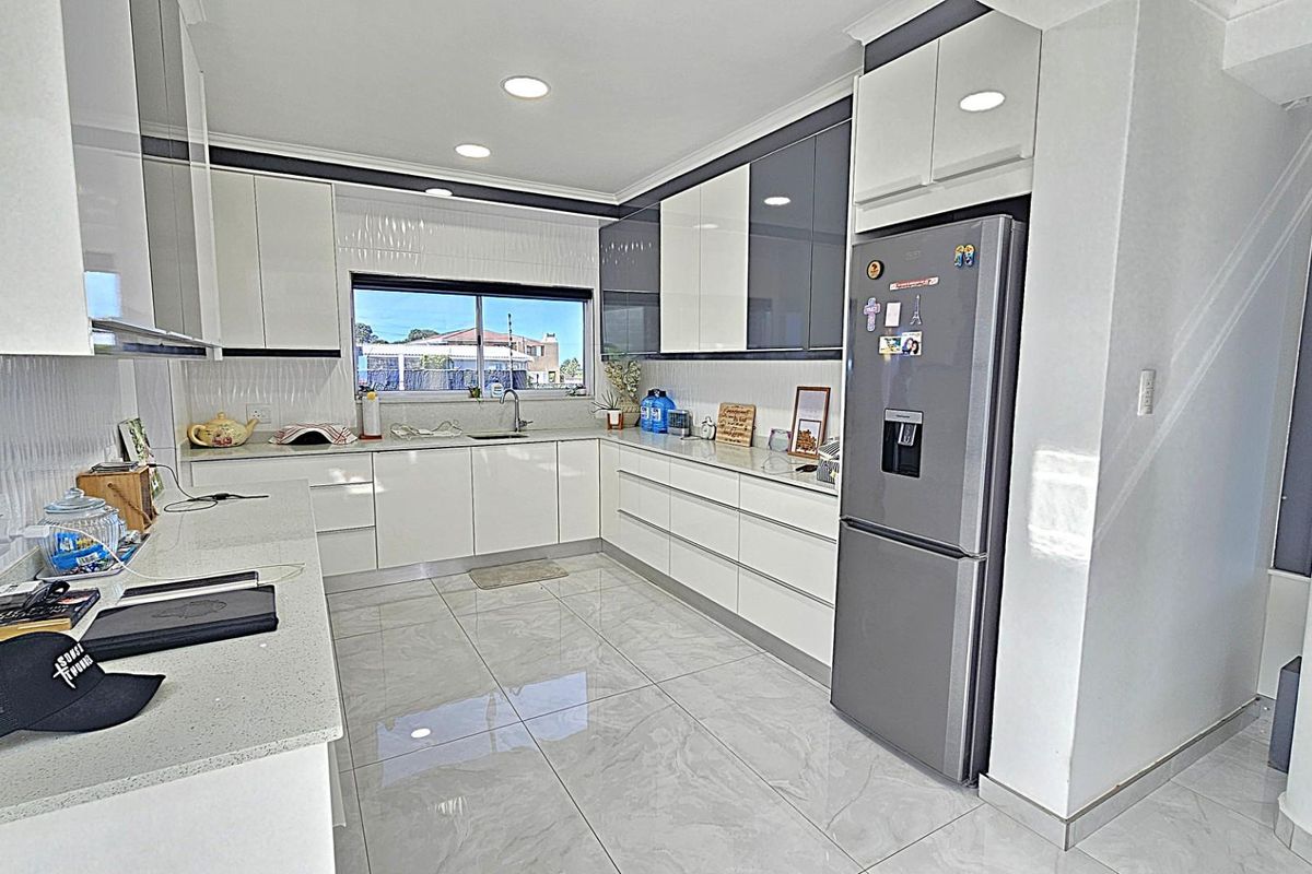 Modern kitchen featuring high-gloss cabinetry, stone countertops, tiled flooring, and recessed lighting, offering a clean and contemporary culinary space.