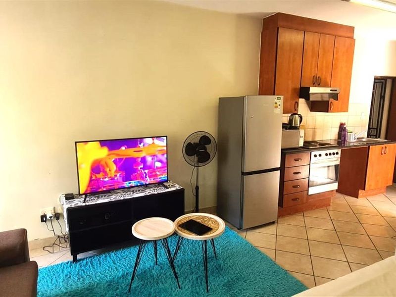 Open-plan living area featuring a compact kitchen with built-in cabinetry, oven, and hob, adjacent to a tiled living space with access to a balcony.
