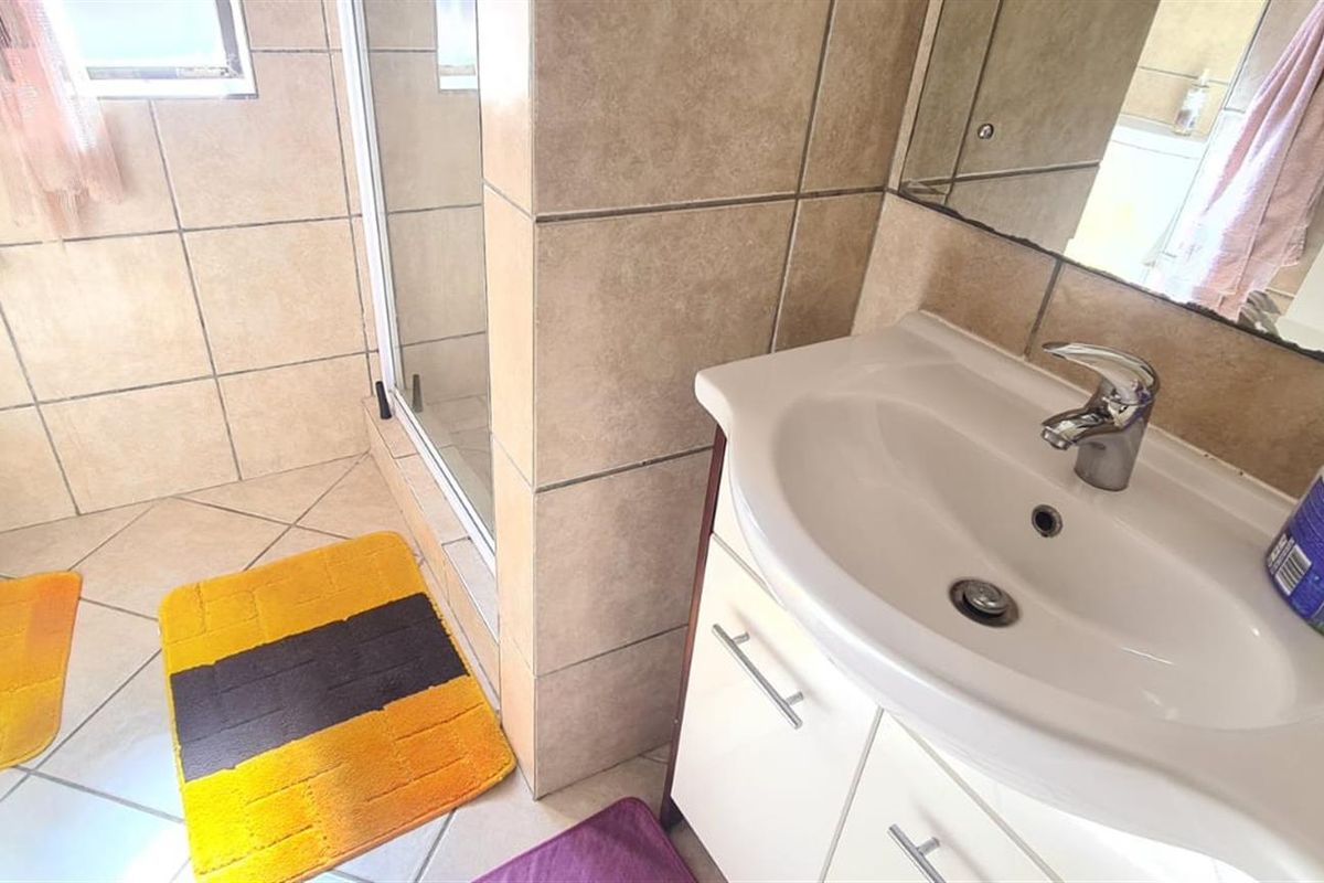 A functional bathroom featuring a vanity cabinet with a basin, a shower enclosure, and tiled finishes throughout.