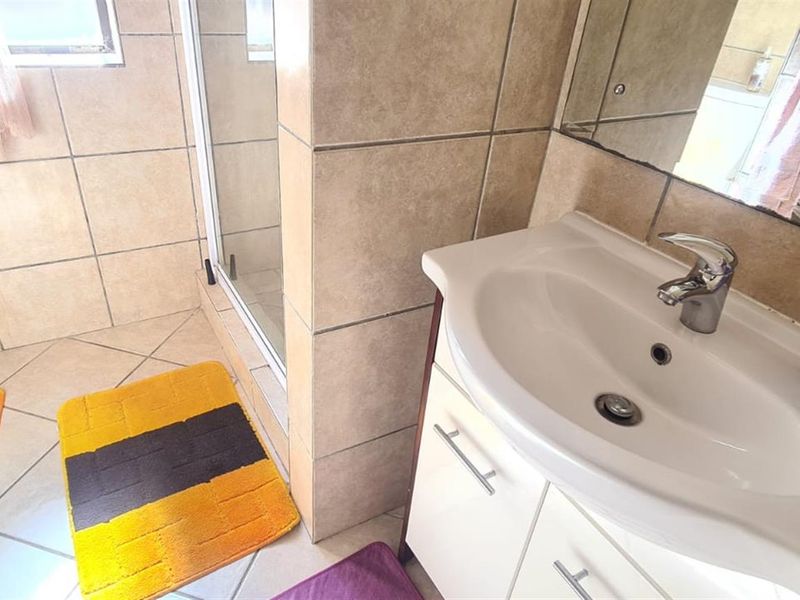 A functional bathroom featuring a vanity cabinet with a basin, a shower enclosure, and tiled finishes throughout.