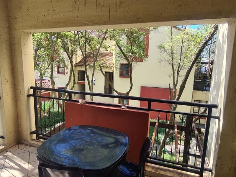 A covered balcony featuring tiled flooring and a metal balustrade, overlooking the complex grounds and parking area.