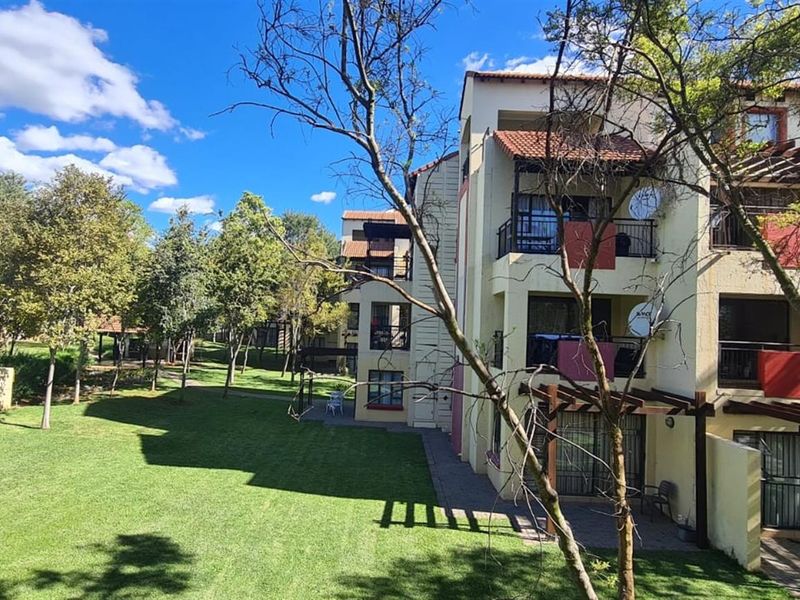 Rear view of the apartment complex featuring multi-level balconies, ground floor patios with timber pergolas, and well-maintained communal garden areas.