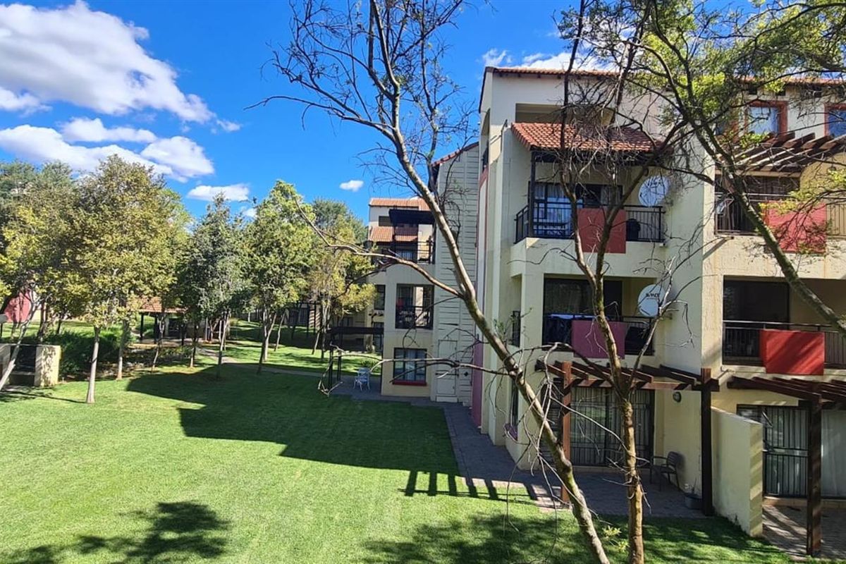 Rear view of the apartment complex featuring multi-level balconies, ground floor patios with timber pergolas, and well-maintained communal garden areas.