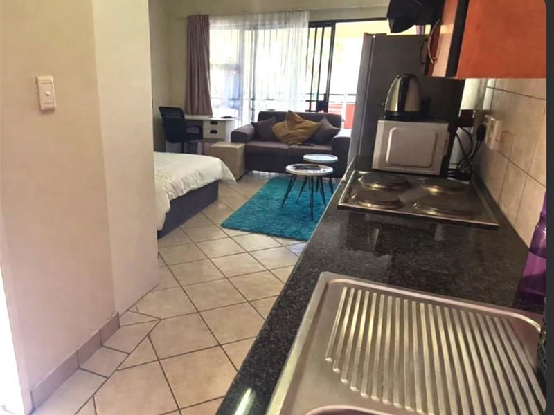 Open plan studio apartment featuring a compact kitchen with granite countertops and tiled flooring, leading into a combined living and sleeping area.