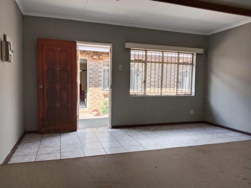 An empty living room featuring tiled flooring, a timber entrance door, and windows fitted with security bars, offering a blank canvas for renovation.