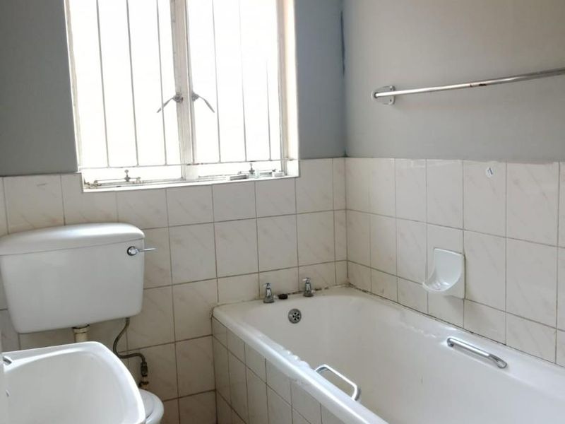 A functional bathroom featuring a standard bathtub, pedestal basin, and toilet, finished with tiled walls and flooring, ready for modernization.