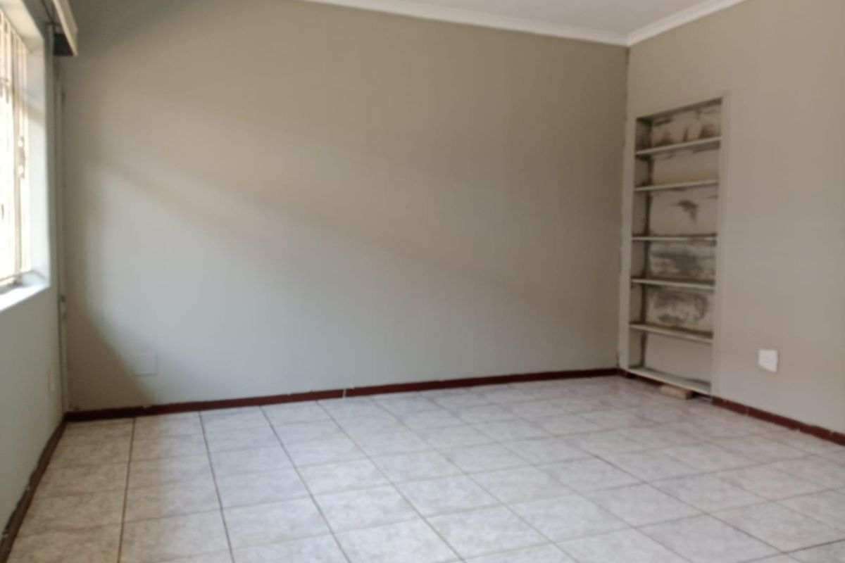 An empty bedroom featuring tiled flooring, neutral walls, and built-in shelving, offering a blank canvas for personalization.