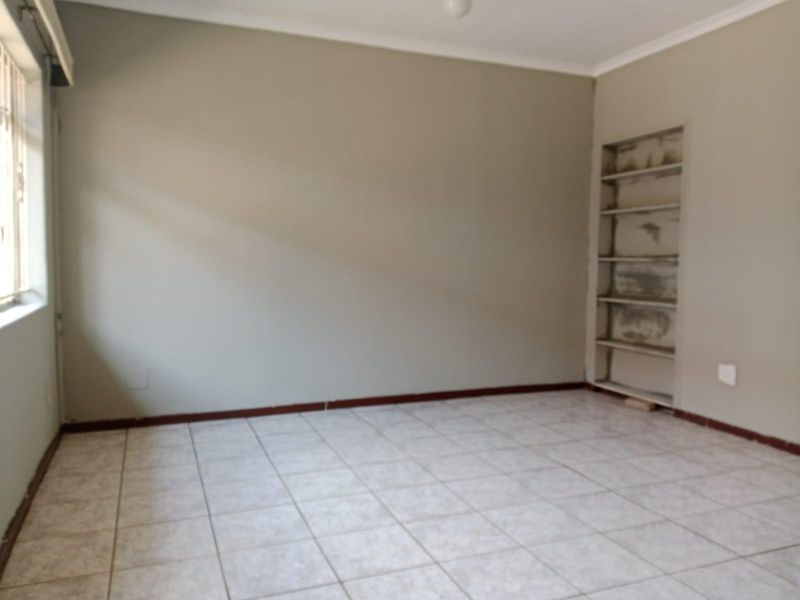 An empty bedroom featuring tiled flooring, neutral walls, and built-in shelving, offering a blank canvas for personalization.