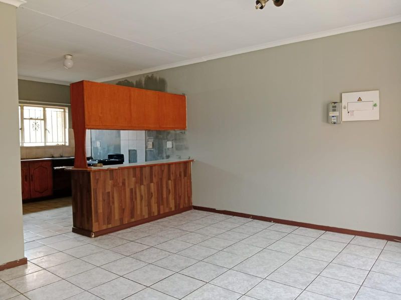 Open plan living and kitchen area featuring tiled flooring, breakfast bar, and built-in cabinetry, requiring minor cosmetic updates to the wall finishes.