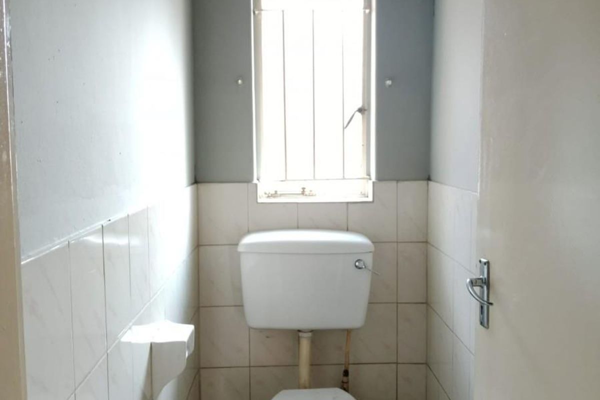 A compact, functional guest toilet featuring tiled walls and flooring, a standard white toilet suite, and a window with security bars.
